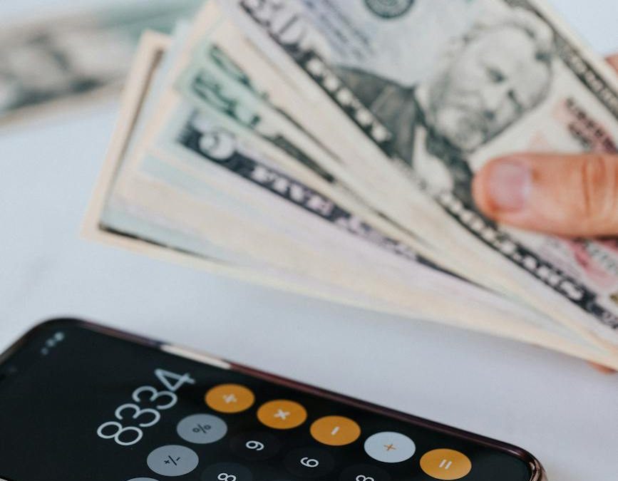 crop unrecognizable person with pile of banknotes calculating on smartphone